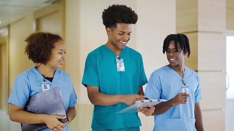 Image of three healthcare workers wearing scrubs talking in hospital hallway