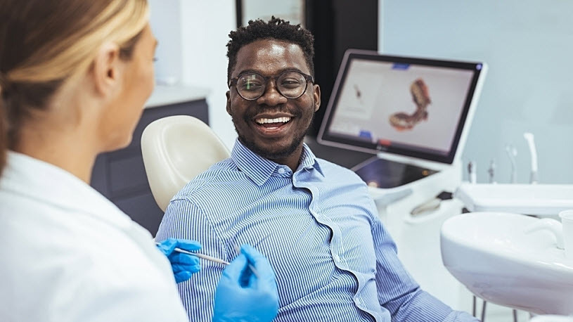 Young Black man sits in dentist's exam chair with woman dentist