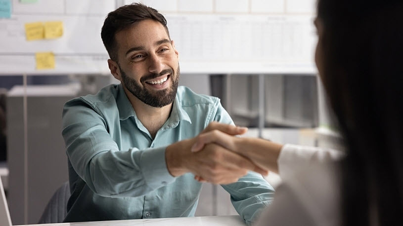 smiling bearded male employee shakes female teammate's hand