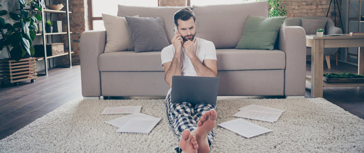 man sitting on living room floor on phone with laptop and papers man sitting on living room floor on phone with laptop and papers