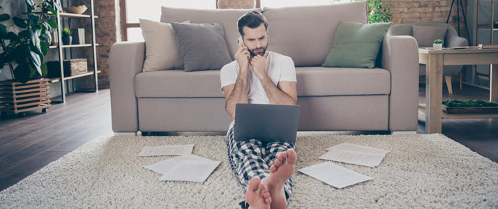 man sitting on living room floor on phone with laptop and papers