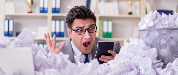 An accountant expresses shock as he holds a calculator above a pile of strewn papers.