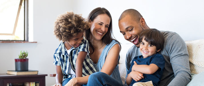Benefits of paid parental leave Happy multiethnic family sitting on sofa laughing together