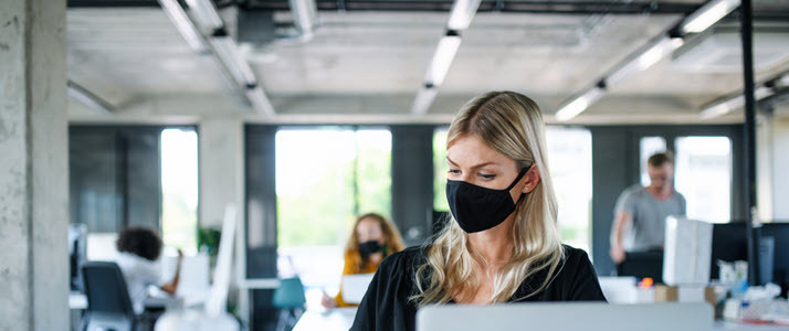 A young woman with a face mask works in an office