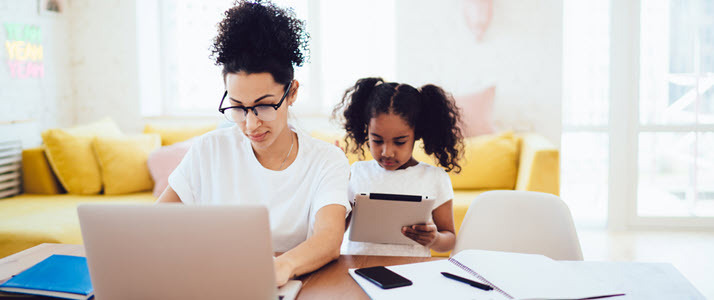 A Black woman works from home on a laptop with daughter by her side