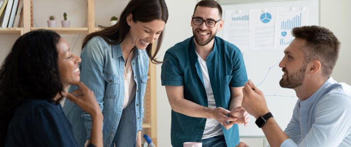 A group of four employees laughing and working together in an office