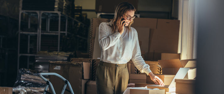 Female small business owner talks to a customer on the phone Female small business owner talks to a customer on the phone while standing in a dimly-lit office
