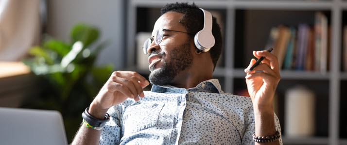 Black guy sits at home office desk wearing headphones with laptop