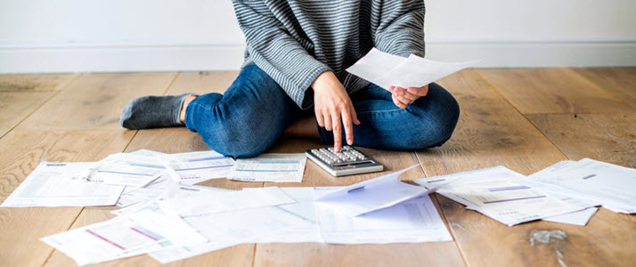 woman sitting on the floor with calculator and bills scattered