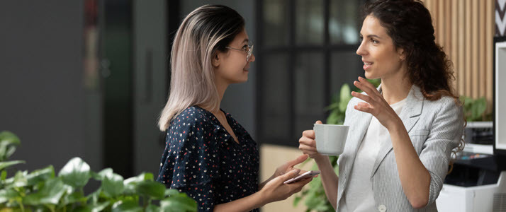 How to Empower Team Leaders to Support Employee Engagement Two young diverse business women chatting during work break standing in modern office