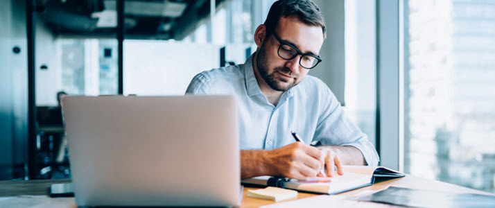 man working at desk making notes with laptop man working at desk making notes with laptop