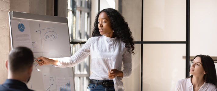 A business woman stands at a white board giving a talk to her colleagues