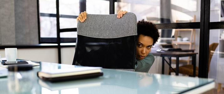 Black female employee hiding behind desk chair