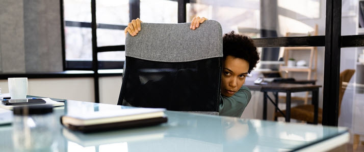 Black female employee hiding behind desk chair Black female employee hiding behind desk chair