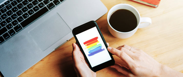 mobile phone in hand displaying rainbow colors laptop on table mobile phone in hand displaying rainbow colors laptop on table