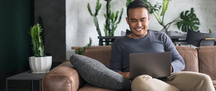 Happy Asian heritage man working on laptop home sofa
