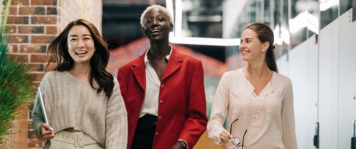 An ethnically diverse trio of femalepresenting professionals walking through an office setting