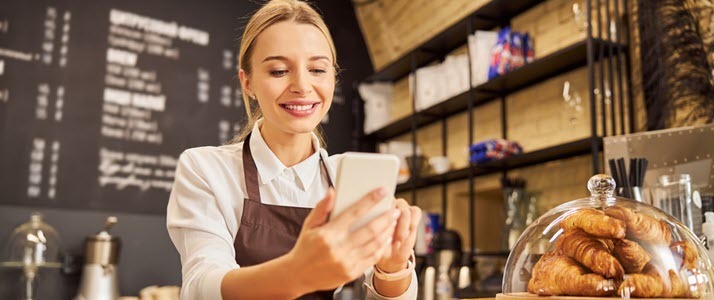 Young woman working at bakery counter checking smart phone