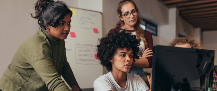 Three women software engineers work on a project together at a computer