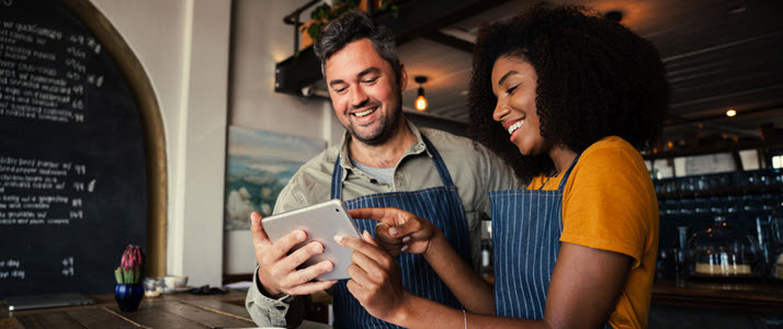 Two smallbusiness employees look at a tablet device together while smiling