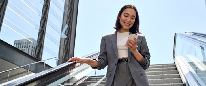 Smiling young woman on office steps looking at smartphone