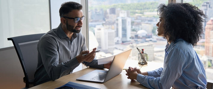 young businessman across desk from young woman talking young businessman across desk from young woman talking