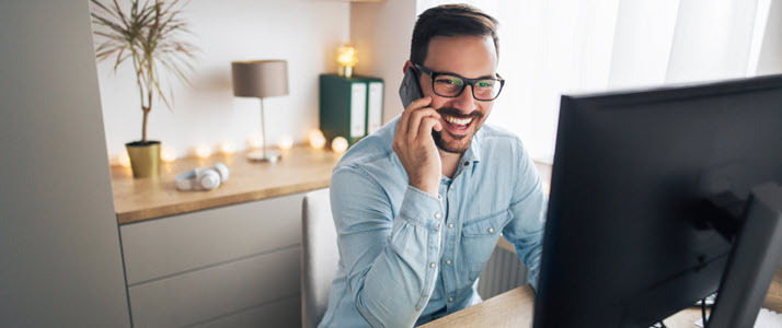 smiling white man at home office desk talking on mobile phone