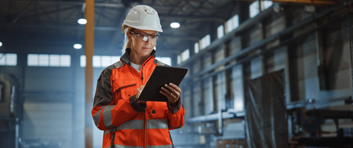 Female worker in a hard hat on job site documents work on tablet