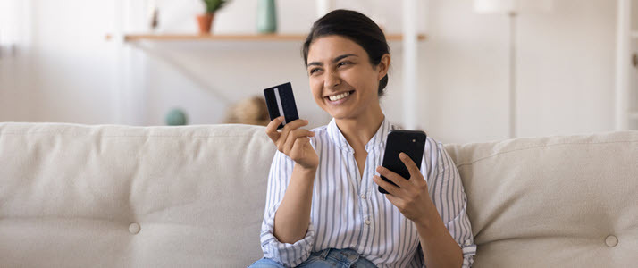 young woman at home paying bills with payment card using phone