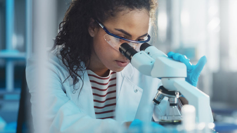 young Black woman looking through a microscope for research