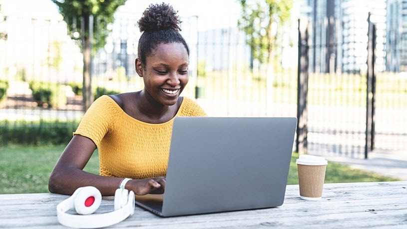 young Black woman works on laptop outside in a park