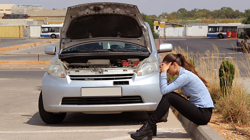 Decorative image - a woman waits on curb beside broken-down car Decorative image - a woman waits on curb beside broken-down car