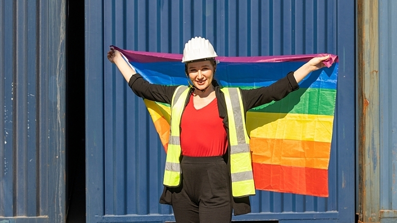 Young female engineer wearing helmet and holding up a PRIDE flag