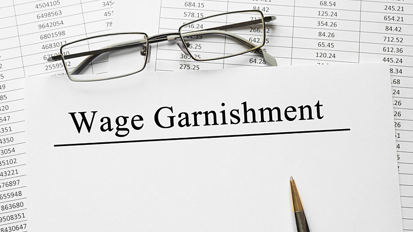 image of pen, reading glasses, spreadsheet and wage garnishment words typed on paper