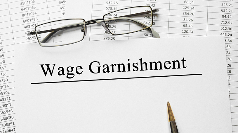 wage garnishment compliance image of pen, reading glasses, spreadsheet and wage garnishment words typed on paper