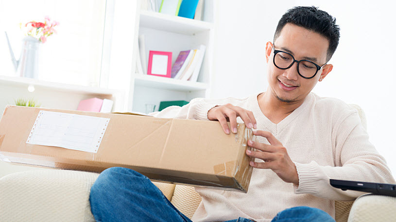 Young Asian man sitting on sofa at home opening a box