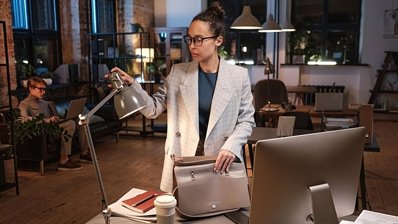 Young female business owner turns light off at desk with computer Young female business owner turns light off at desk with computer