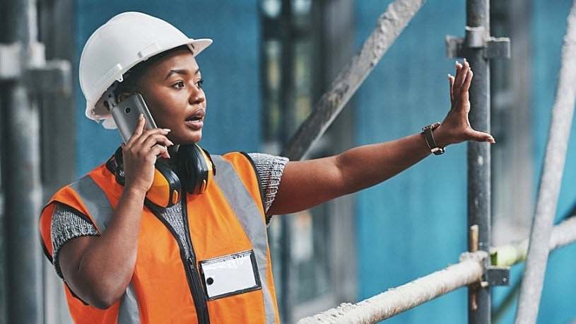 Young Black woman on job site wearing hard hat talking on radio A hard-working woman on a construction job site