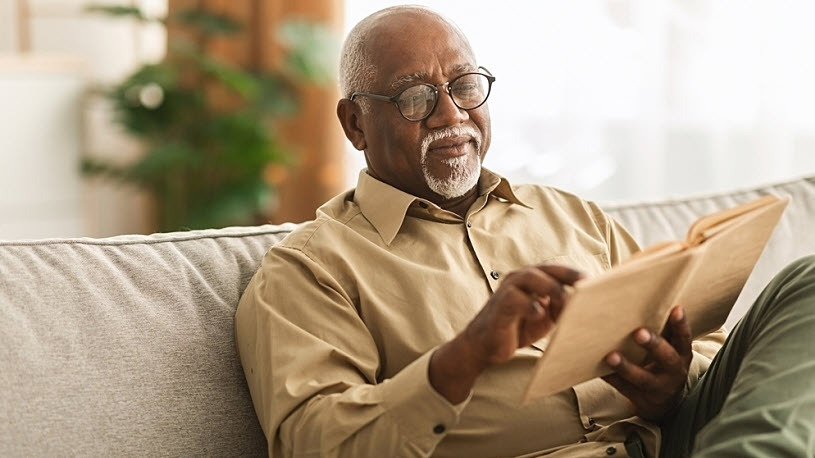 senior Black man sitting on couch reading a book senior Black man sitting on couch reading a book
