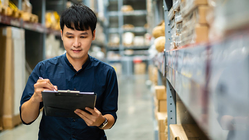 Young Asian man in warehouse with clipboard checking inventory Young Asian man in warehouse with clipboard checking inventory