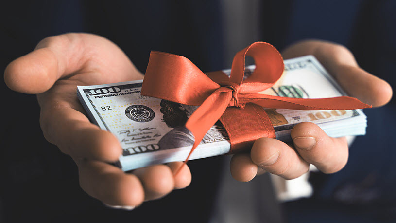 open hands holding stack of cash tied with a red bow