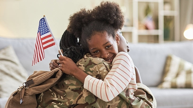 Daughter embracing Veteran mother holding American flag Portrait of Black little daughter with American flag embracing her mom in military uniform