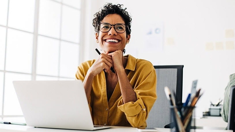 Smiling Black woman at desk with computer looking up