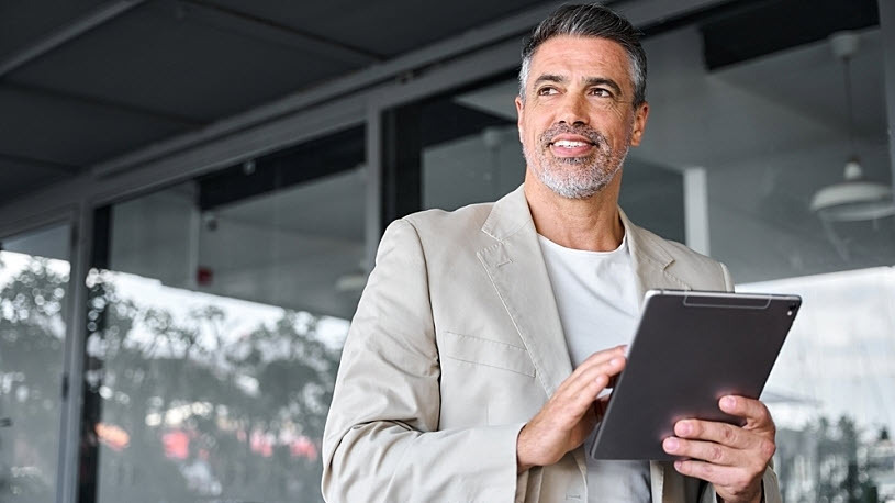 smiling mid aged business man holding digital tablet Compensation Benchmarking is Required Competitive Intelligence