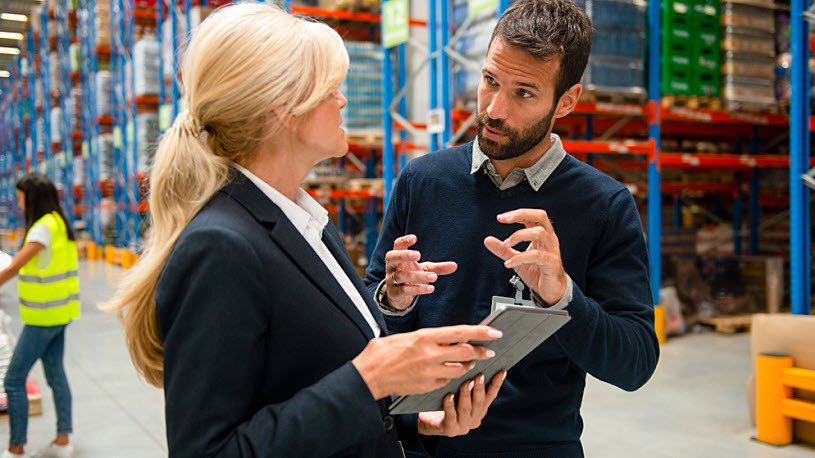HR Data Analytics A male and female manager discuss people analytics on computer tablet in warehouse space