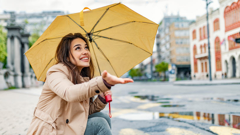 Image of young woman under umbrella holding hand out to feel rain