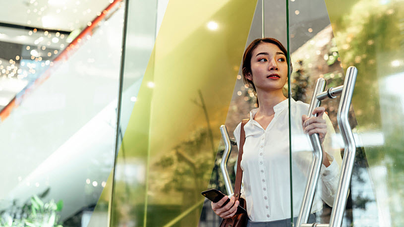 AI in the Workplace Young woman opens glass door to modern office building looking aside