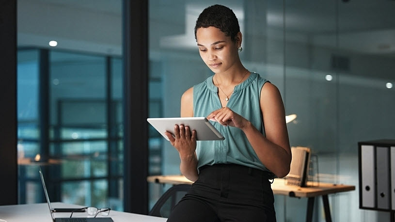 Generative AI A businessperson in their office uses a tablet while leaning against their desk.