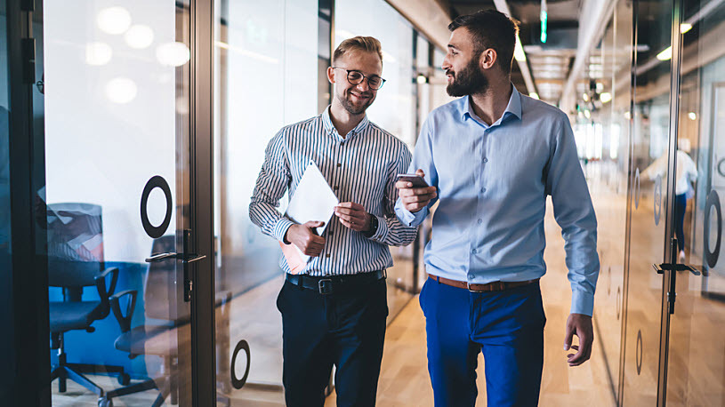 Young male coworkers walking and talking in small business hall Young male coworkers walking and talking in small business hall