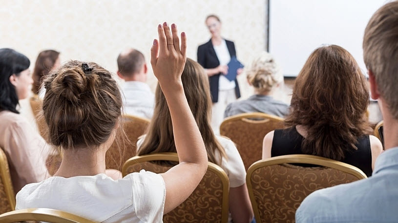 female professional with raised hand asks question in meeting